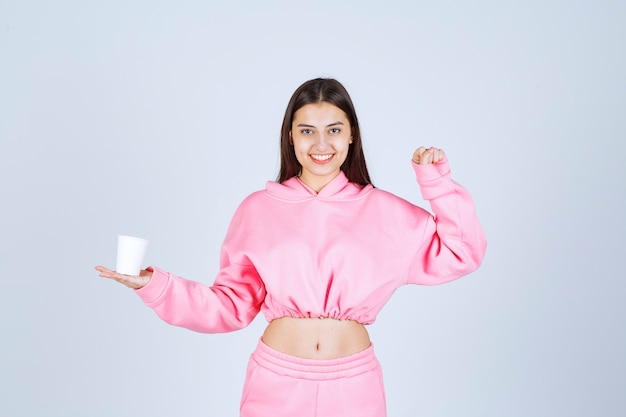 Girl in pink pajamas holding a coffee cup and showing her fist