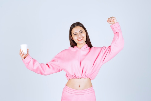 Girl in pink pajamas holding a coffee cup and showing her fist