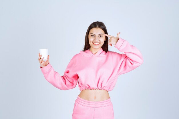 Девушка в розовой пижаме держит чашку кофе и думает