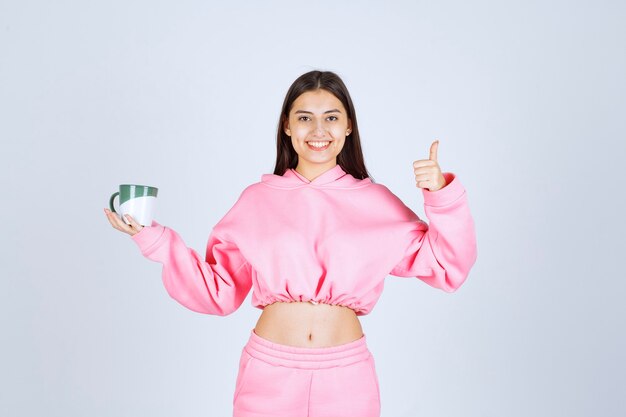 Girl in pink pajamas holding a coffee mug and enjoying the taste. 