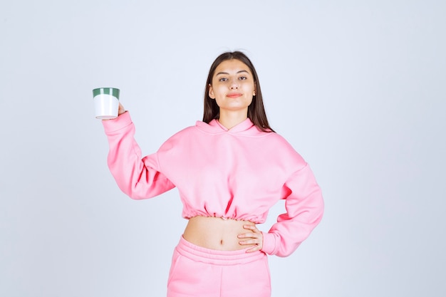 Girl in pink pajamas holding a coffee mug and feeling happy. 