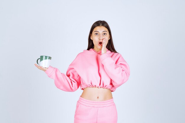 Girl in pink pajamas holding a coffee mug and looks surprized. 