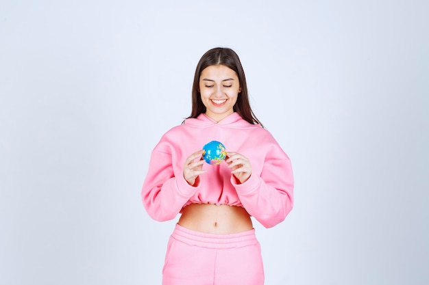 Девушка в розовой пижаме держит в руке мини-глобус.