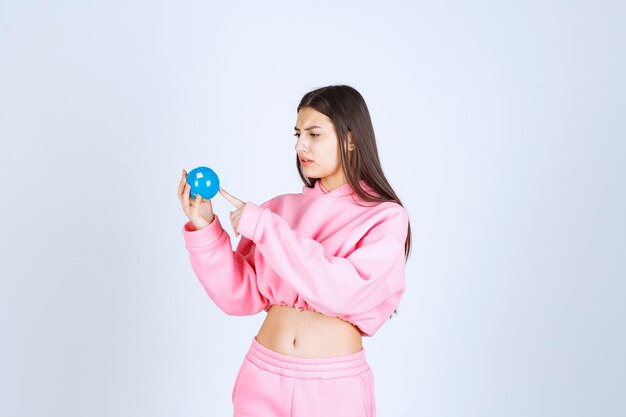 Girl in pink pajamas holding a mini globe and pointing somewhere at it. 