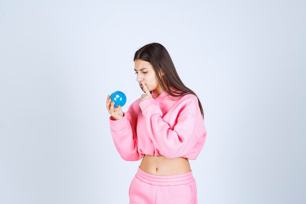 Girl in pink pajamas holding a mini globe and thinking. 