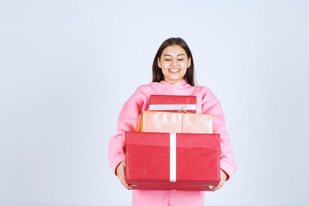 Girl in pink pajamas holding multiple red gift boxes and feeling happy. 