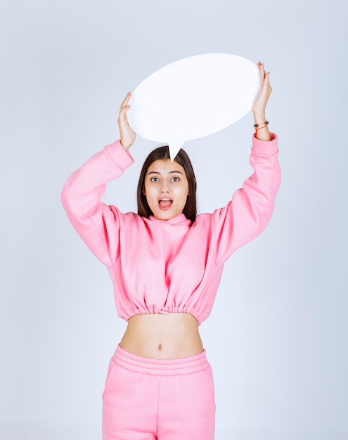 Girl in pink pajamas holding a round think board over her head. 