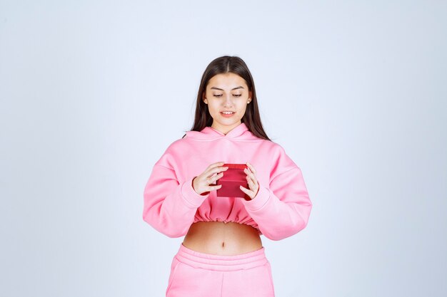 Girl in pink pajamas holding a small red gift box. 