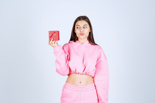 Girl in pink pajamas holding a small red gift box. 