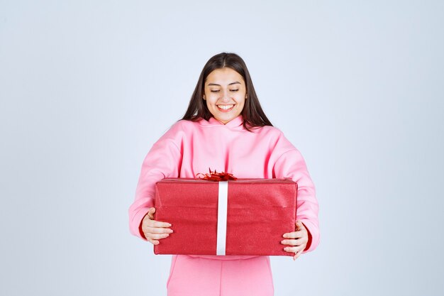 Girl in pink pajamas hugging a big red gift box and smiling. 