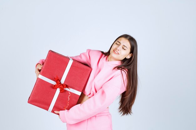 Girl in pink pajamas hugging a big red gift box and smiling. 