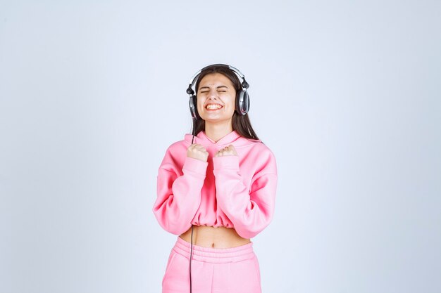 Girl in pink pajamas listening the headphones and having fun. High quality photo