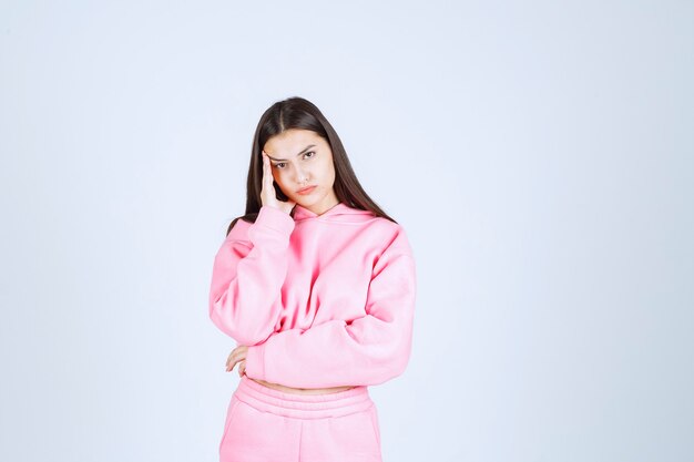 Girl in pink pajamas looks confused and thoughtful. 