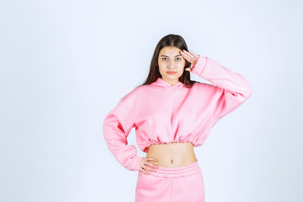 Girl in pink pajamas putting fingers to her forehead