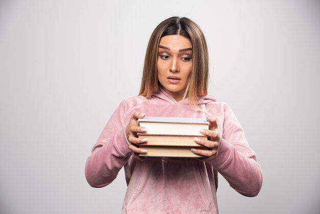 Girl in pink swaetshirt holding and carrying heavy pile of books.