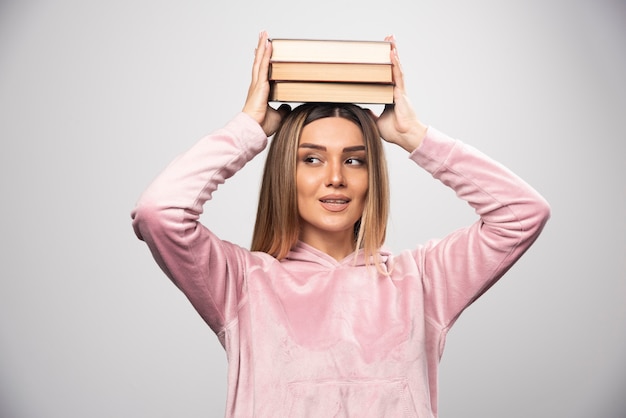 Girl in pink swaetshirt holding her books over her head.