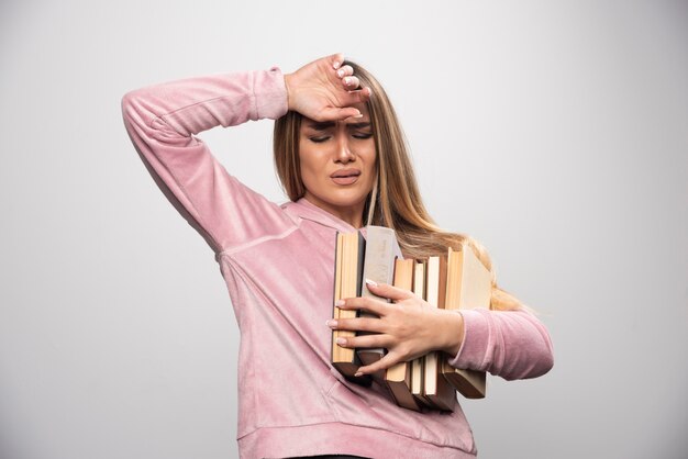 Girl in pink swaetshirt holding a stock of books and feels tired.