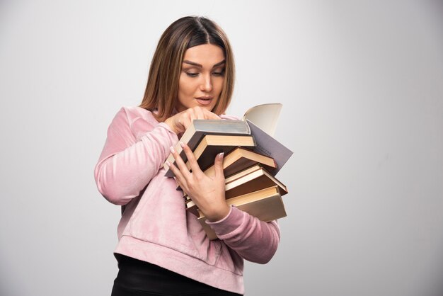 Girl in pink swaetshirt holding a stock of books and trying to read the top one with a magnifier