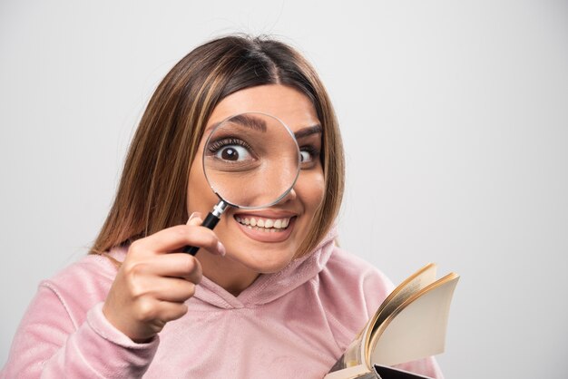 Girl in pink swaetshirt putting a magnifier to her eye and looking through it