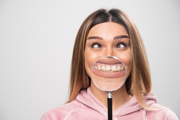 Foto gratuita ragazza in swaetshirt rosa che mette una lente d'ingrandimento alla sua bocca