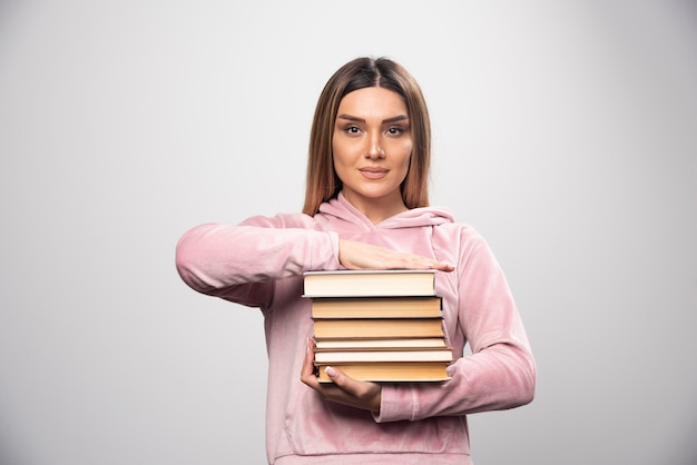 Girl in pink sweatshirt holding and carrying heavy pile of books.