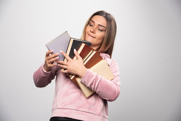 Girl in pink sweatshirt holding and carrying heavy pile of books.