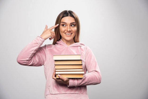 Girl in pink sweatshirt holding a stock of books and feels smart.