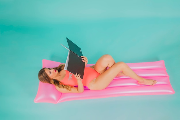 Girl in pink swimsuit reading on pool mattress