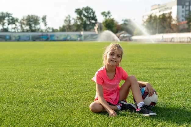 Девушка в розовой футболке сидит на футбольном поле