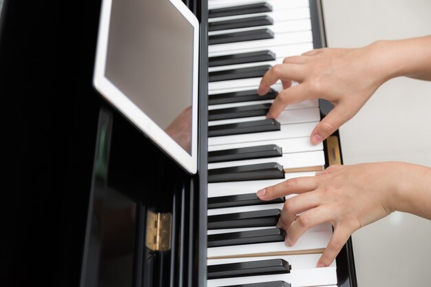 Girl playing piano while reading sheet music from her tablet