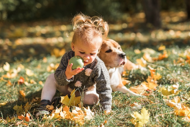 Girl playing with ball sitting in grass near her dog at park