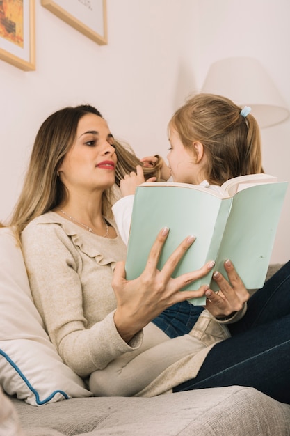 Girl playing with hair of reading mother