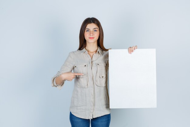 girl pointing at blank canvas in shirt and looking confident.