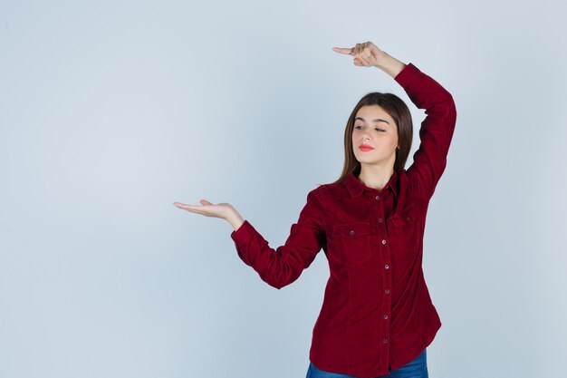 girl pointing left, spreading palm aside in burgundy shirt and looking confident.