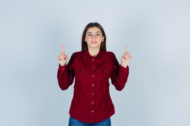 Girl pointing up in burgundy blouse and looking confident.