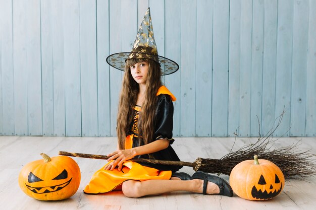 Girl in pointy hat sitting on floor with pumpkins