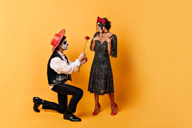 Girl in polka dot dress with flowers in her hair is pleasantly surprised by  act of her young man. Guy in sombrero gives red rose to his womang.