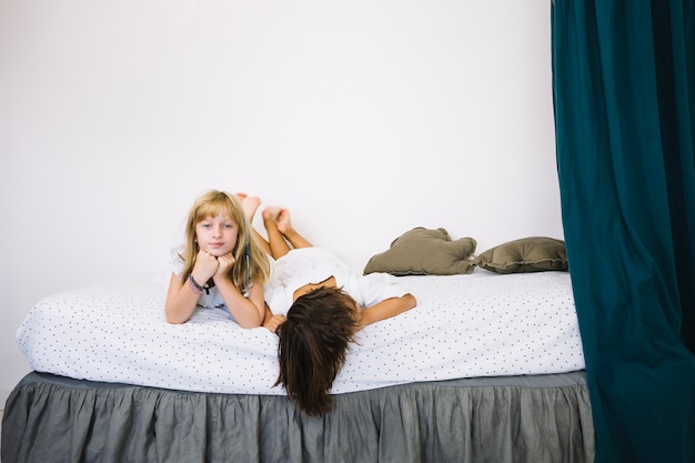 Free photo girl posing on bed near tired sister