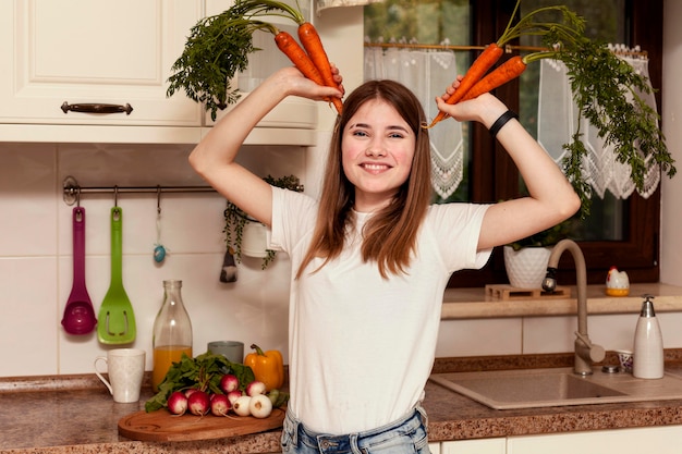 Girl posing with carrots in the kitchen