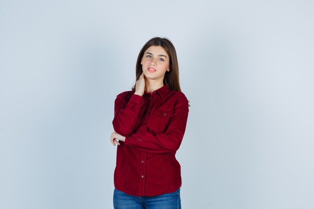 girl posing with hand on neck in burgundy shirt and looking sensible.