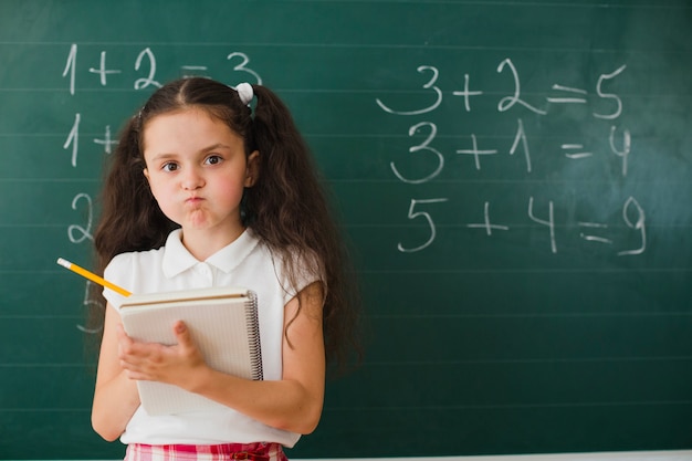 Девушка позирует с блокнотом в математическом классе