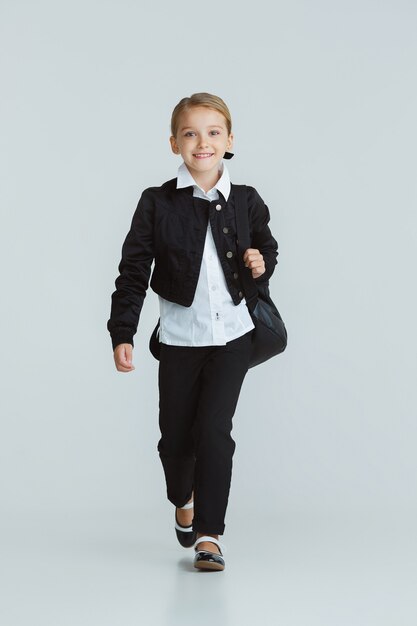 Girl preparing for school after a long summer break. Back to school. Little female caucasian model posing in school's uniform on white  wall. Childhood, education, holidays concept.