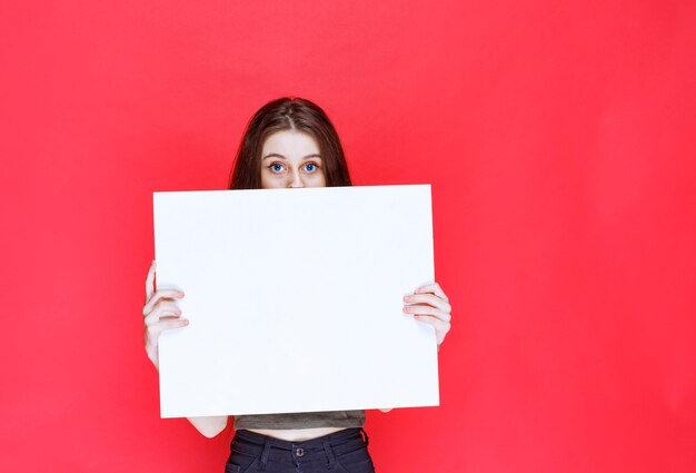 Girl presenting a square info board and looks surprized and confused. 