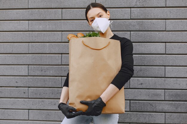 Девушка в защитной маске держит пакет с продуктами