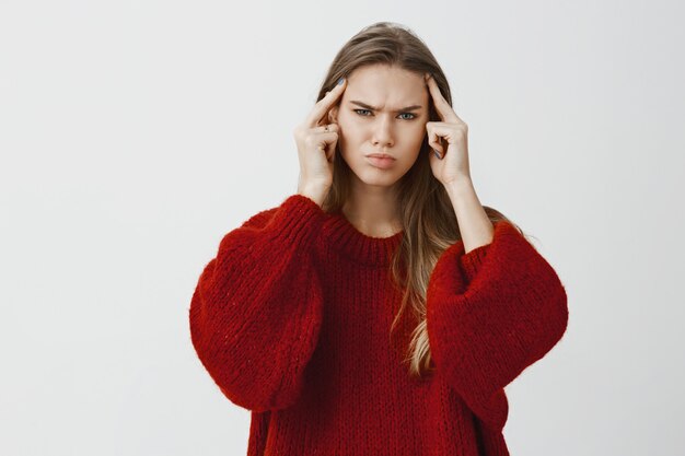 Girl pulling all efforts to find solution or remember something. Portrait of focused troubled young woman, holding index fingers in temples and frowning, trying concentrate on issue over gray wall