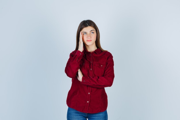 girl pulling skin on her temples, looking up in casual shirt and looking thoughtful