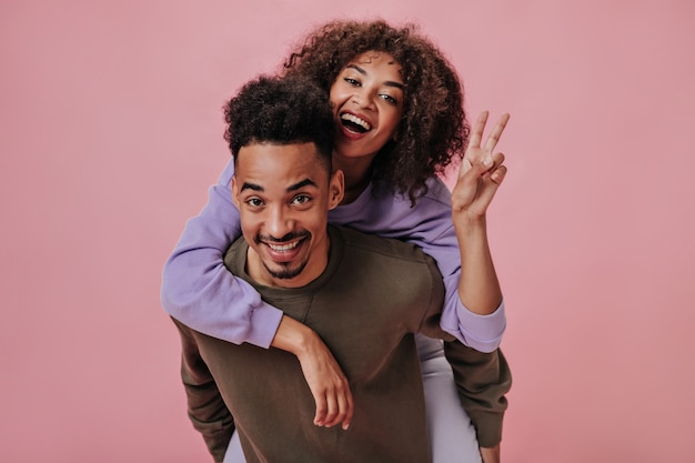 Girl in purple hoodie sitting on her boyfriends back and showing peace sign