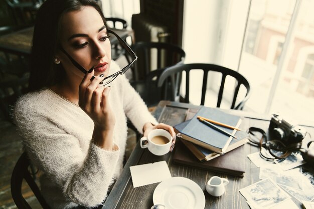 Girl puts on her glasses sitting with cup of coffee in the cafe