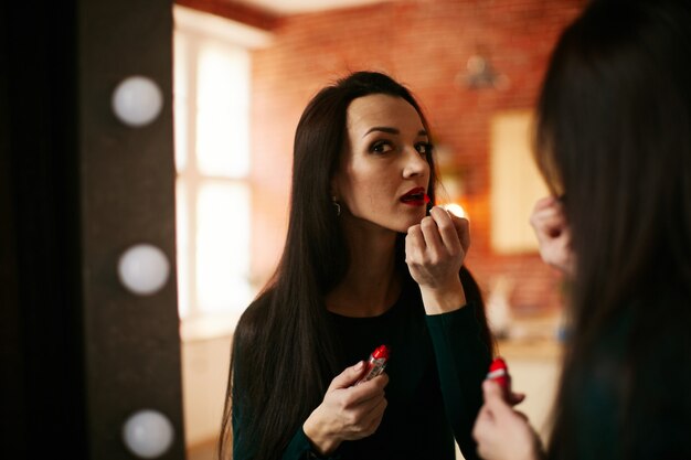 The girl puts a red lipstick on her lips