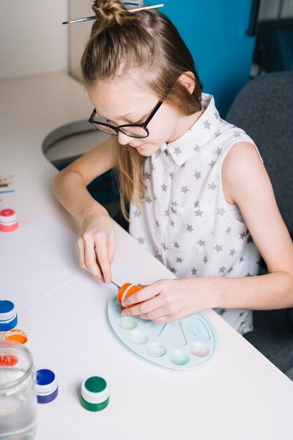 Girl putting gouache on palette at table 